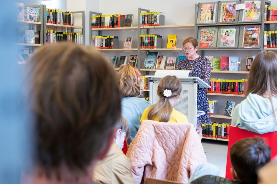 Foto einer Frau am Stehpult, die Zuhörern in der Bücherei etwas vorliest. (C) Andrea Borowski