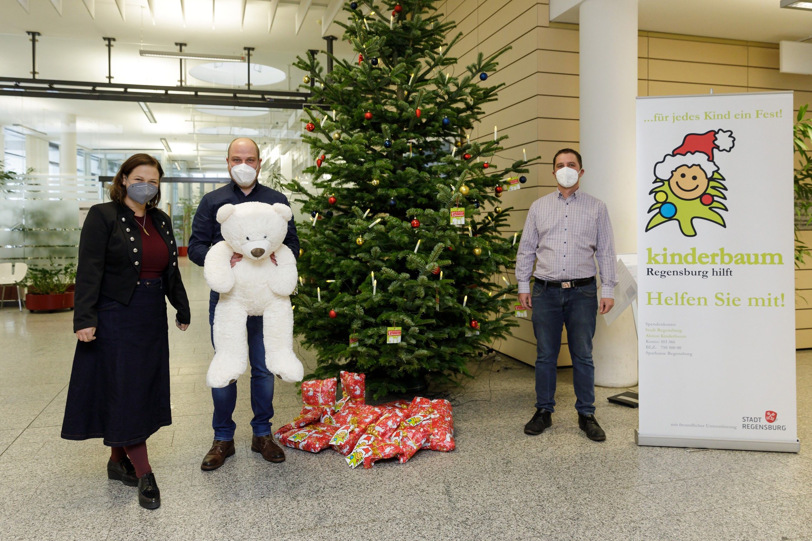 Fotografie - drei Personen neben einem Weihnachtsbaum mit Geschenken