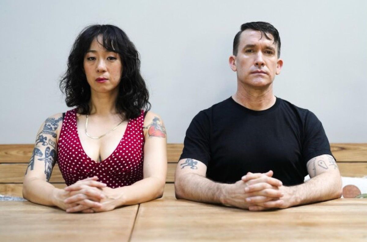 Fotografie - Die Künstler Seo und Stewart sitzend an einem Holztisch