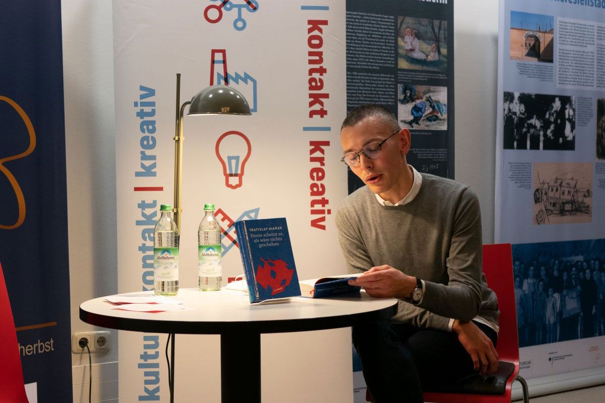 Fotografie – Der Schriftsteller Vratislav Maňák sitzt am Tisch und liest aus seinem Roman