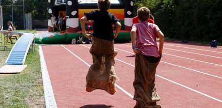 Themenbild Familien - Fotografie - Zwei Kinder beim Sackhüpfen, im Hintergrund eine Hüpfburg  mit Kindern