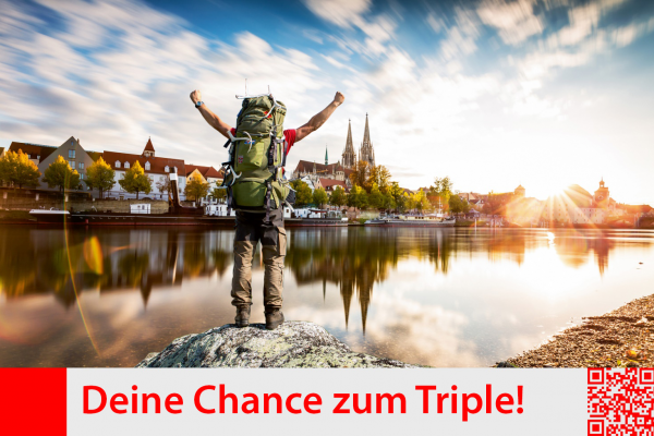 Mann mit großem Rucksack, Arme hoch reißend, Siegerpose; vor ihm die Donau und dahinter Blick auf Regensburg mit dem Dom; blauer Himmel mit weißen Wolken