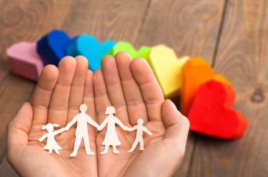 Fotografie: Zwei Hände halten ein Papierstück in Form einer Familie