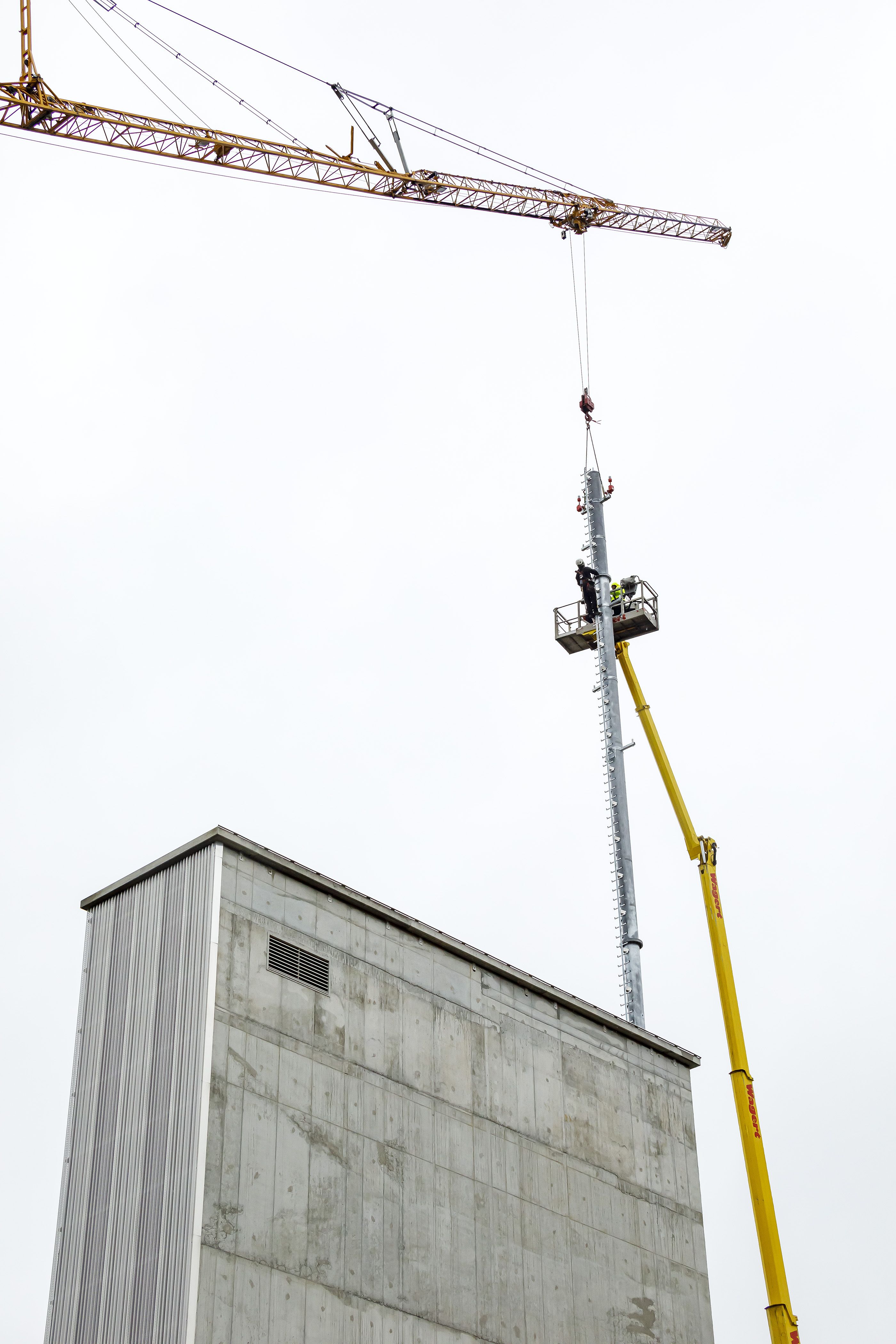 Fotografie - Montage des Funkmastes am Schlauchturm - Funkmastteil wird mittels eines Krans an der richtigen Stelle zur Montage positioniert