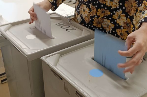 Fotografie: Eine Person wirft Umschläge in zwei Briefwahlurnen.