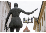 Fotografie: Hinter der Statue des Don Juan d'Austria stehen Arbeiter auf einer Hebebühne und begutachten die Fassade des Alten Rathauses.