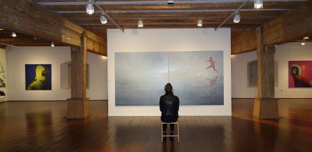 Themenbild Museen - Eine Frau sitzt vor einem großen Gemälde in einer Bilderausstellung