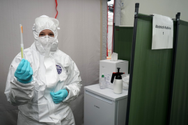 Fotografie: Frau in Schutzkleidung hält Impfstoff in die Höhe