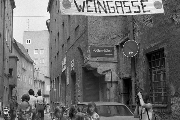 Zu sehen ist eine Aufnahme aus der Weingasse direkt vor dem neuen Jugendzentrum 1977. Quer über die Gasse wurde ein Banner mit der Aufschrift „Jugendzentrum Weingasse“ gespannt.                                    