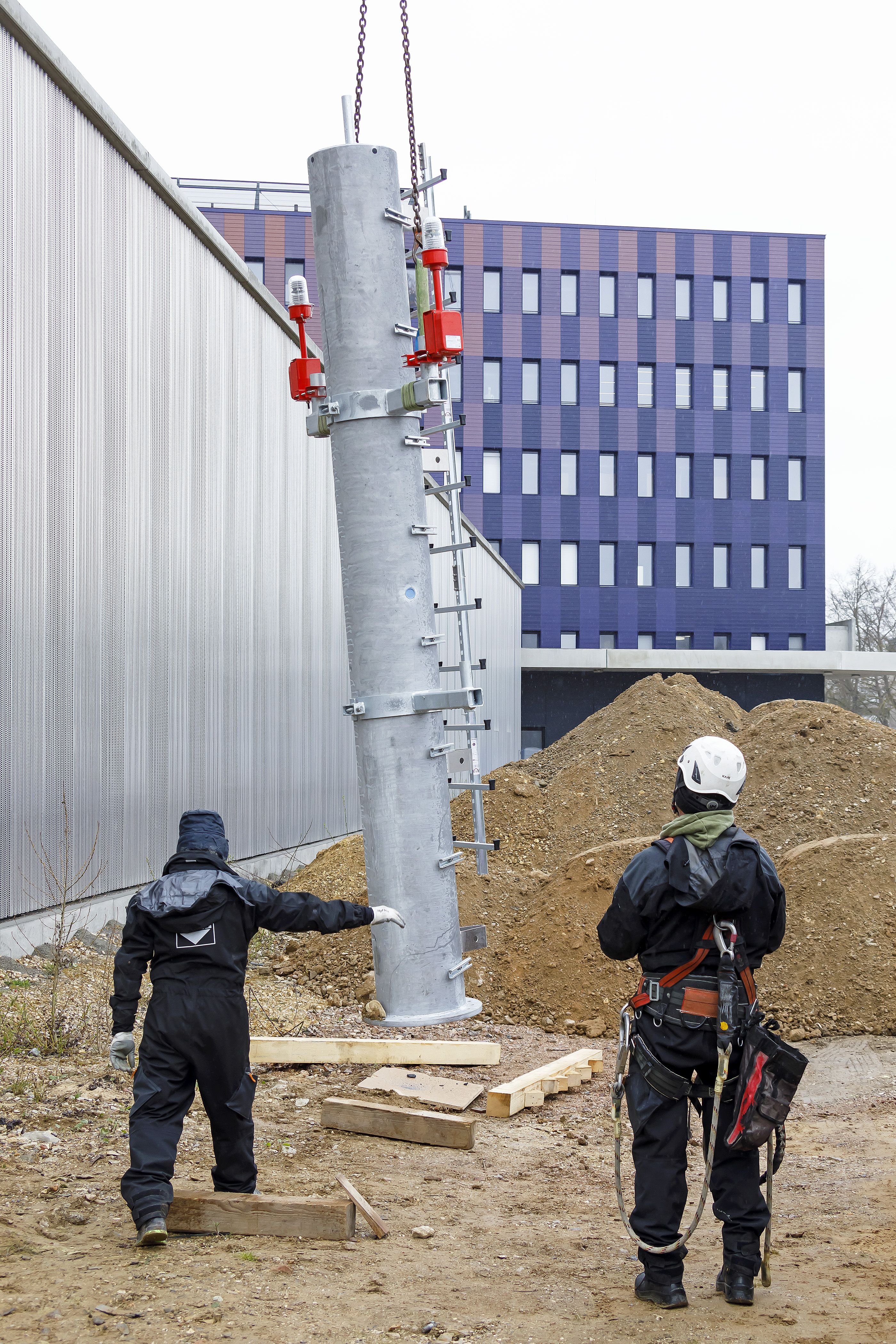 Fotografie - Montage des Funkmastes am Schlauchturm - zwei Mitarbeiter überwachen das Anheben eines Teils des Funkmastes 