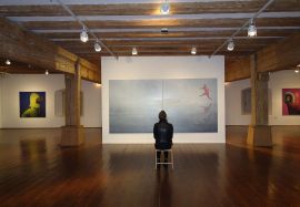 Themenbild Museen - Eine Frau sitzt vor einem großen Gemälde in einer Bilderausstellung