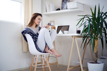 Fotografie – eine Frau sitzt mit angezogenen Beinen auf einem Stuhl und tippt im Handy