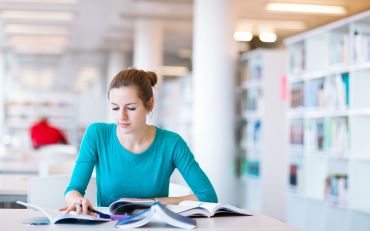 Fotografie: Eine Frau sitzt mit Büchern an einem Tisch.