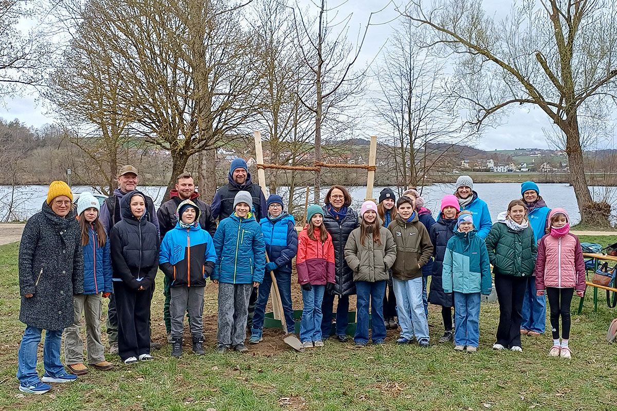 Fotografie - Gruppenbild mit Mitgliedern des Kinderbeirates, Oberbürgermeisterin Gertrud Maltz-Schwarzfischer und Mitarbeiterinnen und Mitarbeitern des Umweltamtes und des Amts für Stadtgrün vor dem neu gepflanzten Baum „Prunus avium“ (gefülltblühende Vogelkirsche) im Donaupark