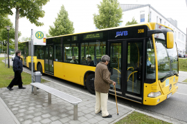 Fotografie - Bus an Bushaltestelle - zwei Personen steigen in den Bus ein