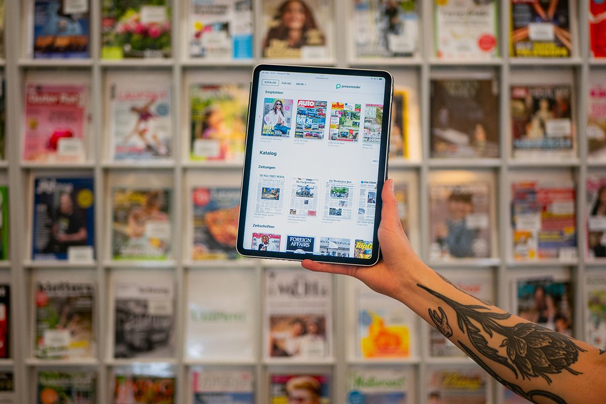 Tablet mit Pressreader App vor dem Zeitschriften-Regal