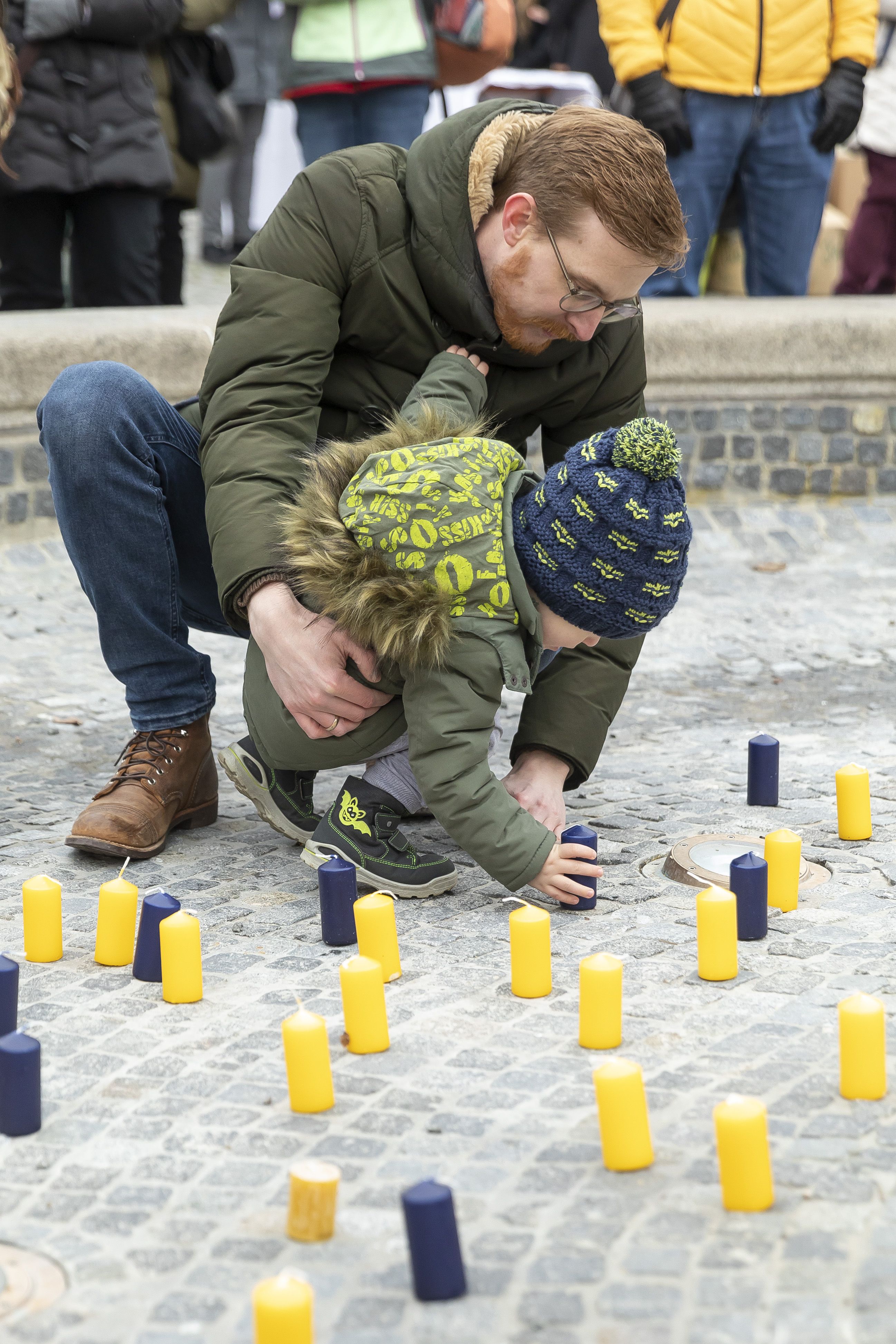 Fotografie: Ein kleiner Junge und ein Mann stellen eine Kerze in den Brunnen am Bismarckplatz.