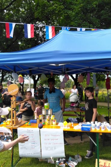 Fotografie - mit Luftballons geschmückter Pavillon und Kinderbeiräte, im Vordergrund Büchsenwerfen