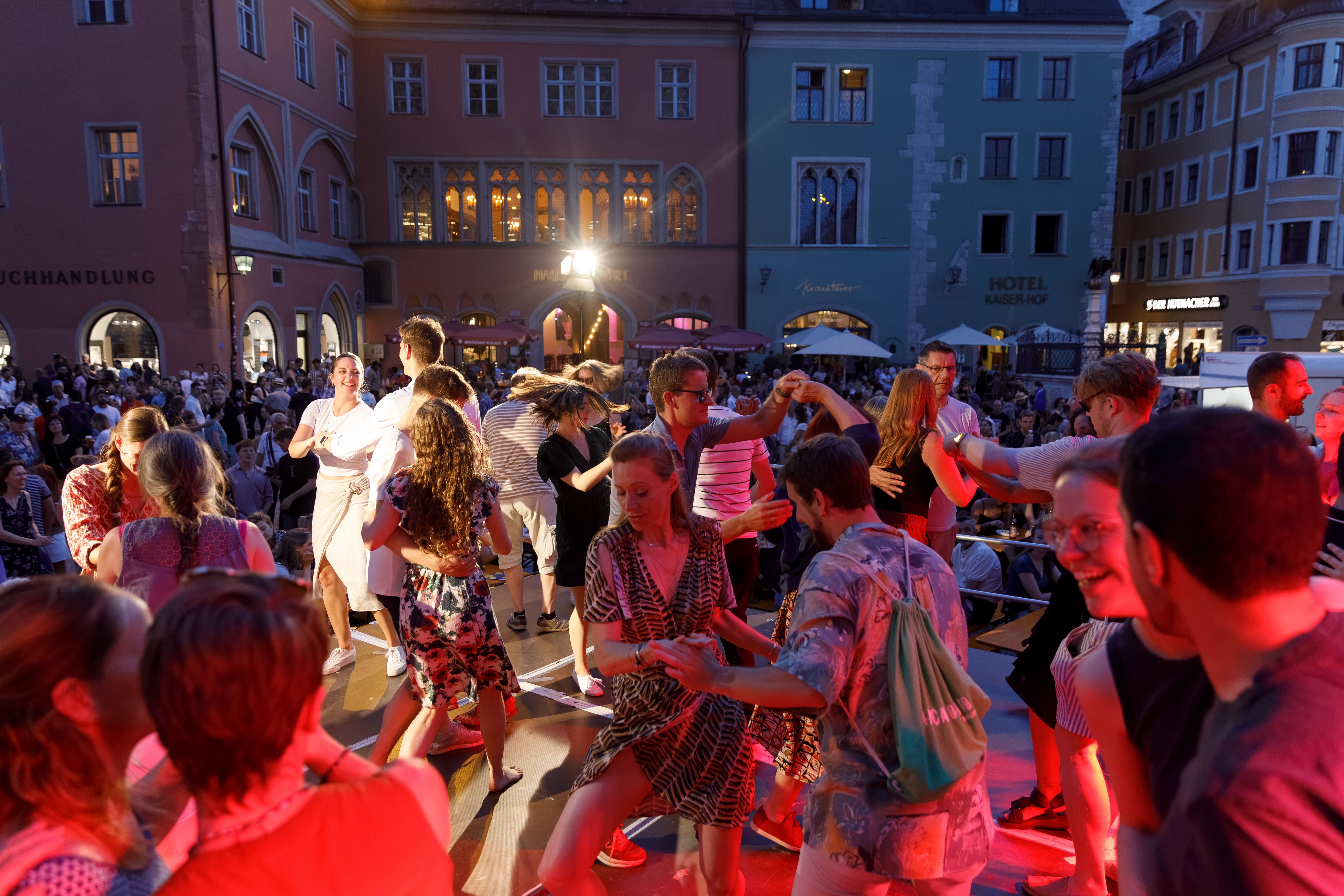 Fotografie: Menschen tanzen auf der rot beleuchteten Bühne vor dem Dom, Westportal
