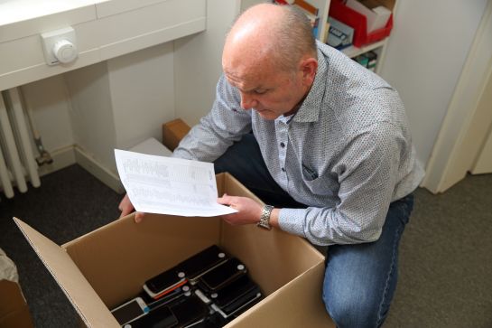 Fotografie: Manfred Stuber schaut in eine Kiste voller Mobiltelefone.