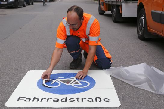 Ein Mitarbeiter der Stadt Regensburg bringt einen Bodenaufkleber "Fahrradstraße" auf der Fahrbahn auf.  (C) Bilddokumentation Stadt Regensburg
