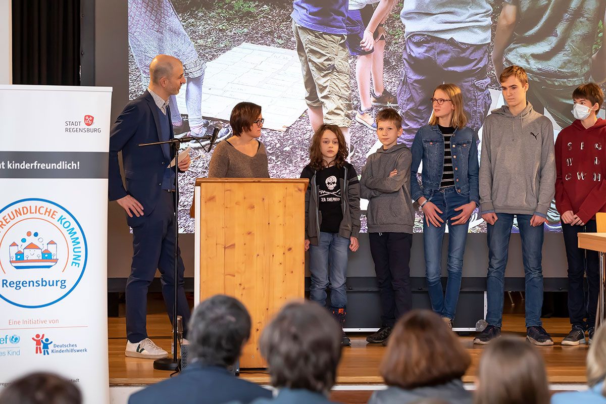 Fotografie – Dominik Bär, Geschäftsführer des Vereins Kinderfreundliche Kommunen, befragt auf der Bühne die Kinderbeiräte Bela, Dominik, Pauline, Jimi-Luke und Maximilian