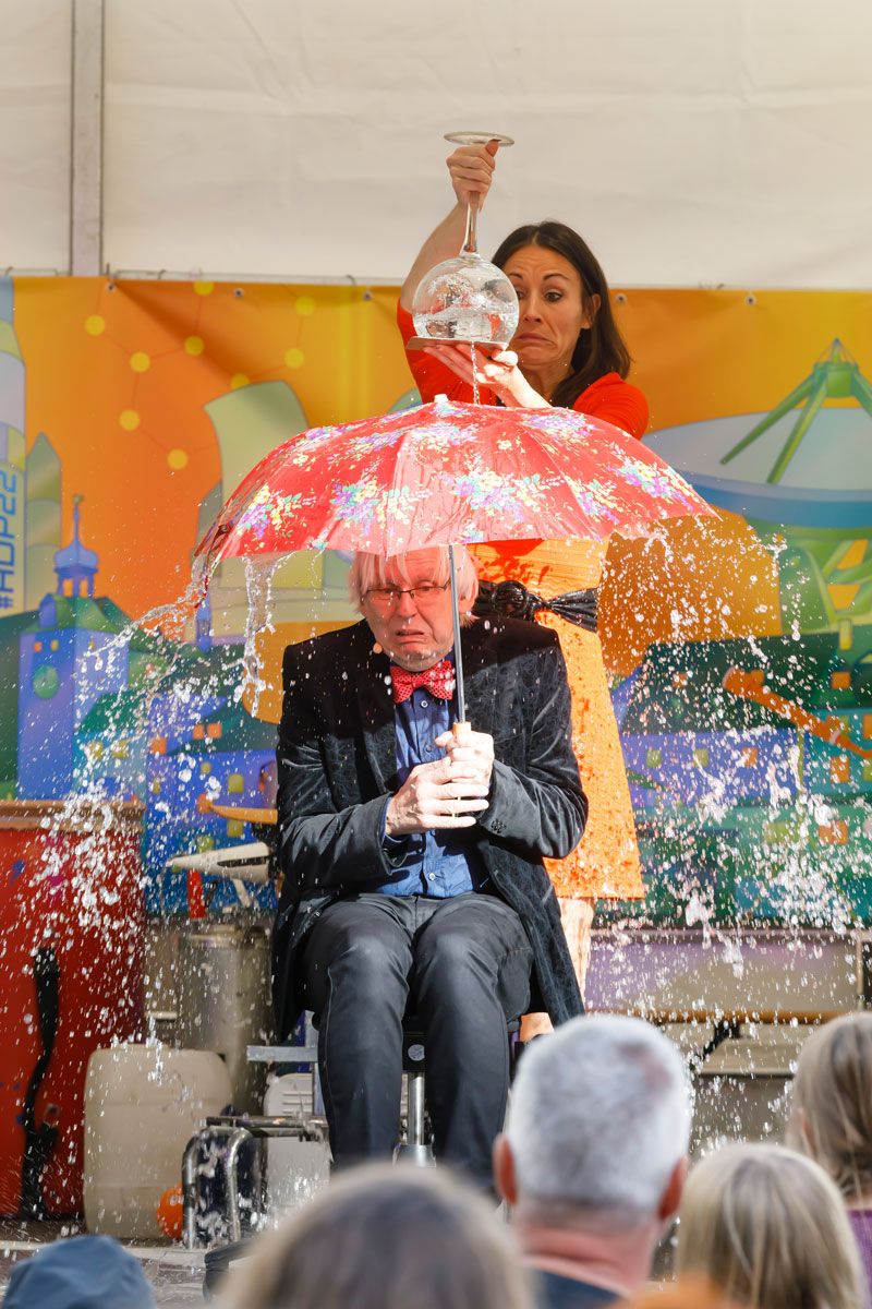 Fotografie: Ein Mann sitzt unter einem Regenschirm und wird mit Wasser übergossen.