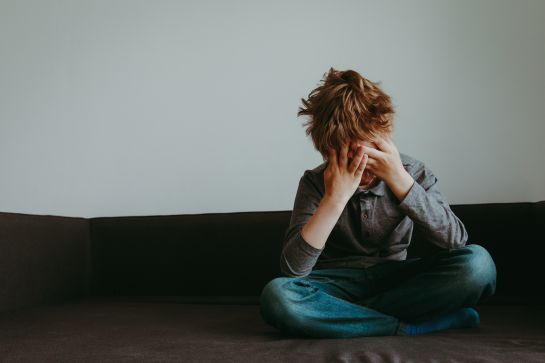 Fotografie: Ein Kind sitzt in verzweifelter Position auf einem Sofa.