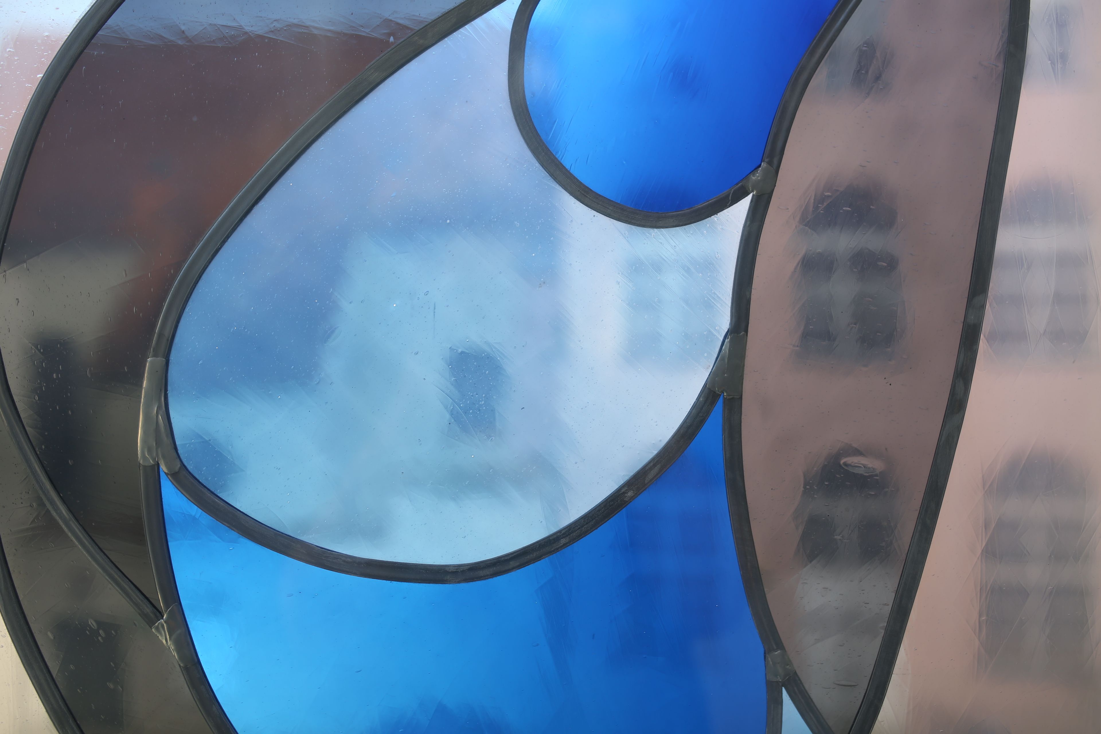 Vordergrund: Buntglasscheibe mit blauen, modernen Ornamenten. Durch die Scheibe hindurch ist das rosane Mehrgenerationenhaus zu sehen.