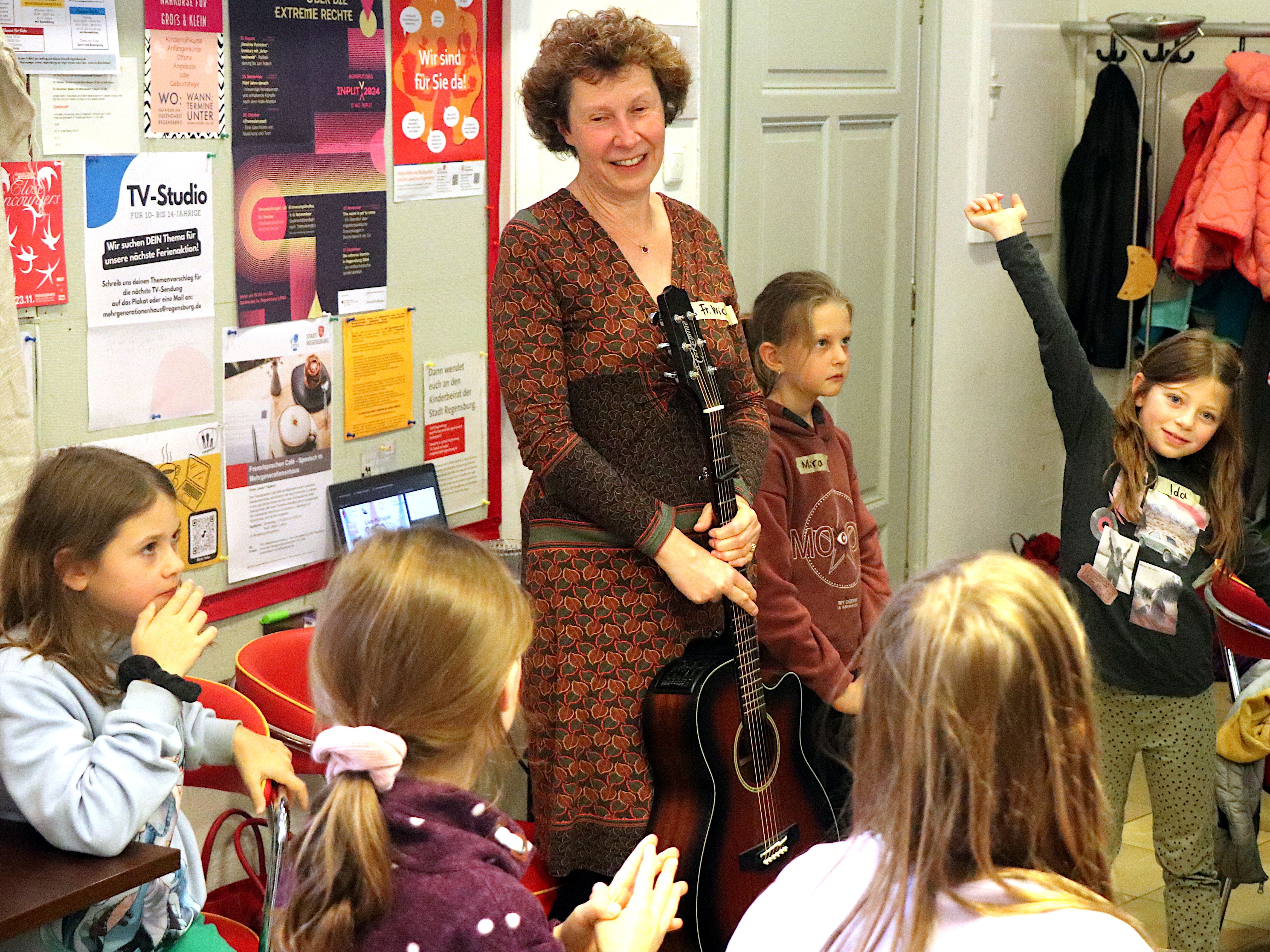 Henriette Wich steht mit einer Gitarre umringt von Kindern im Café Klara