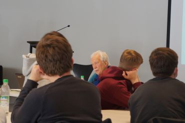 Menschen in einem Raum hören einem Mann, Ernst Grube, zu.
