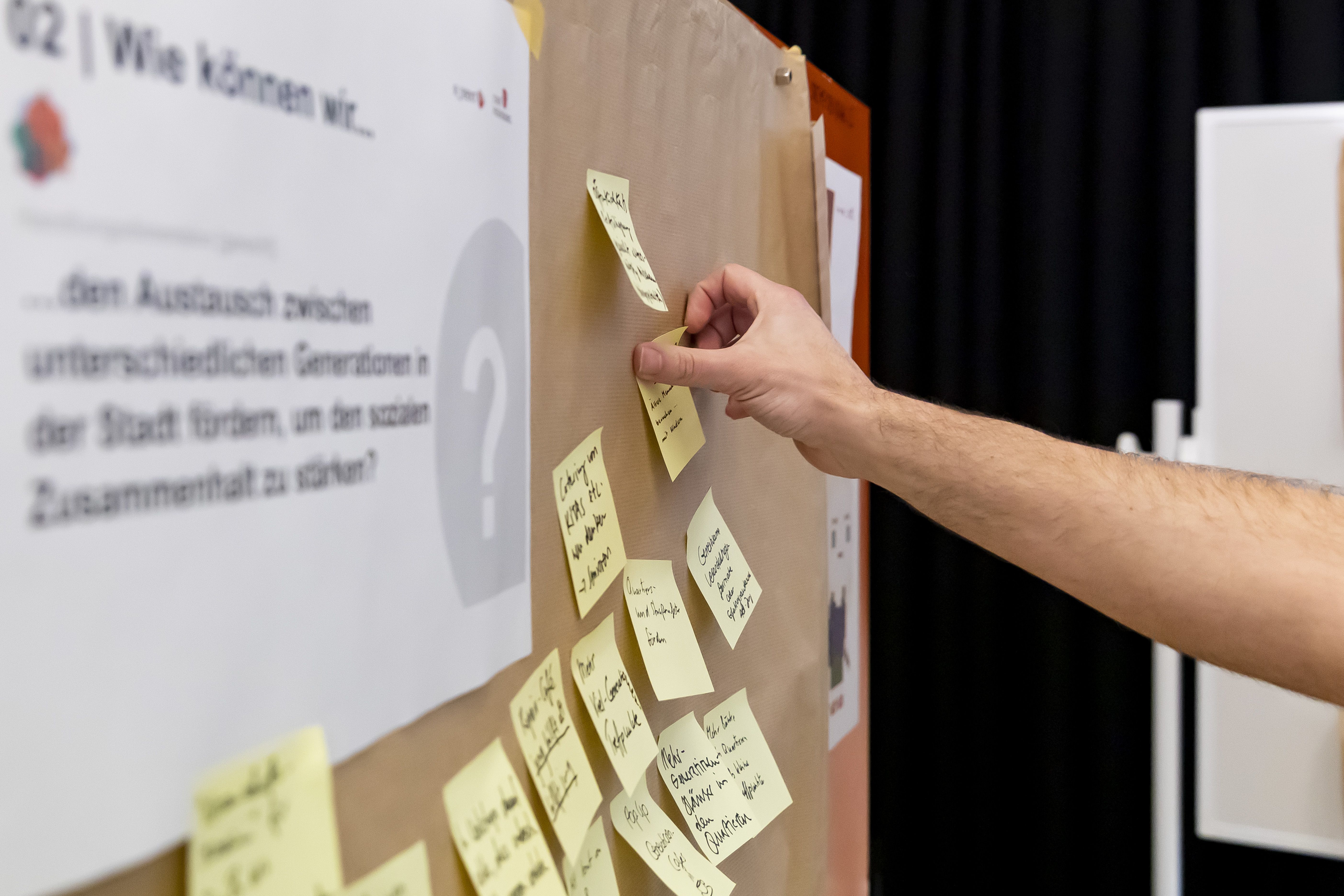 Ein Besucher klebt ein Post-it mit einer Idee an eine Pinnwand.