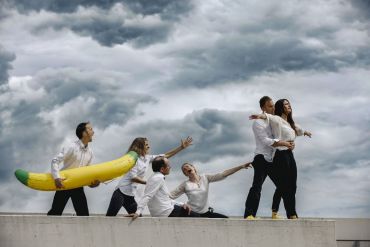 Fotografie: Impro Theater Gruppe von 6 Personen auf einem Dach mit wolkigem Himmel und Plastikbanane