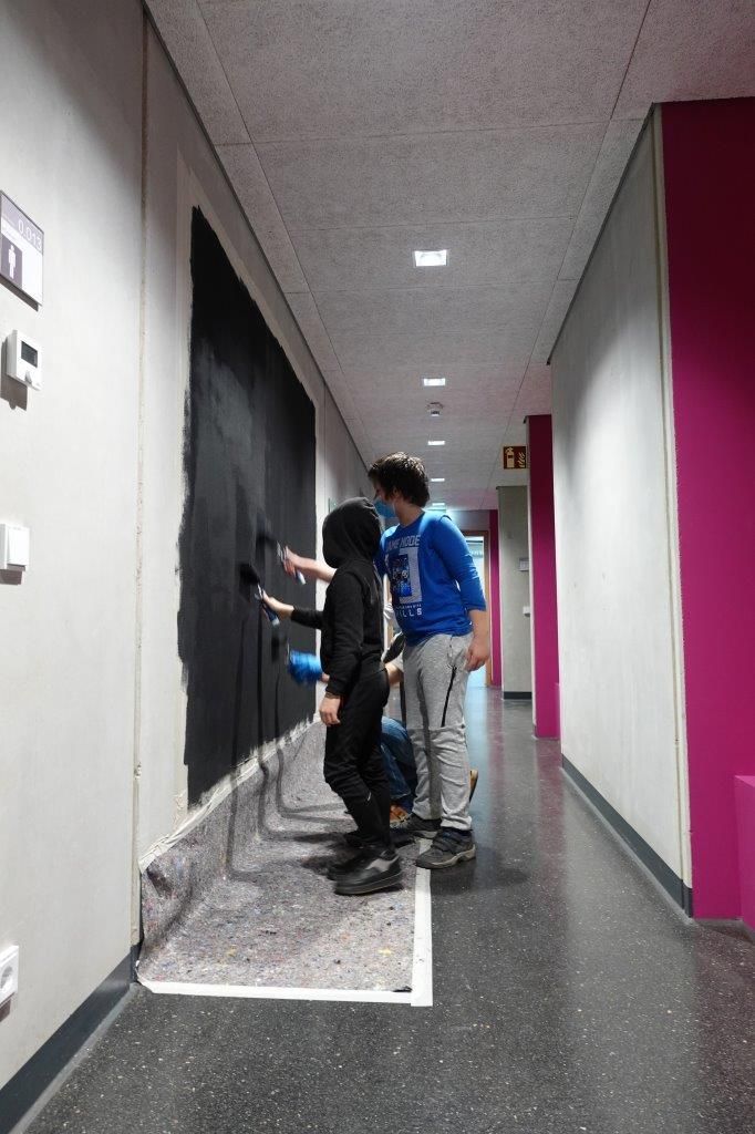 Auf dem Foto sind zwei Kinder und eine erwachsene Person zu sehen, welche eine Wand streichen.