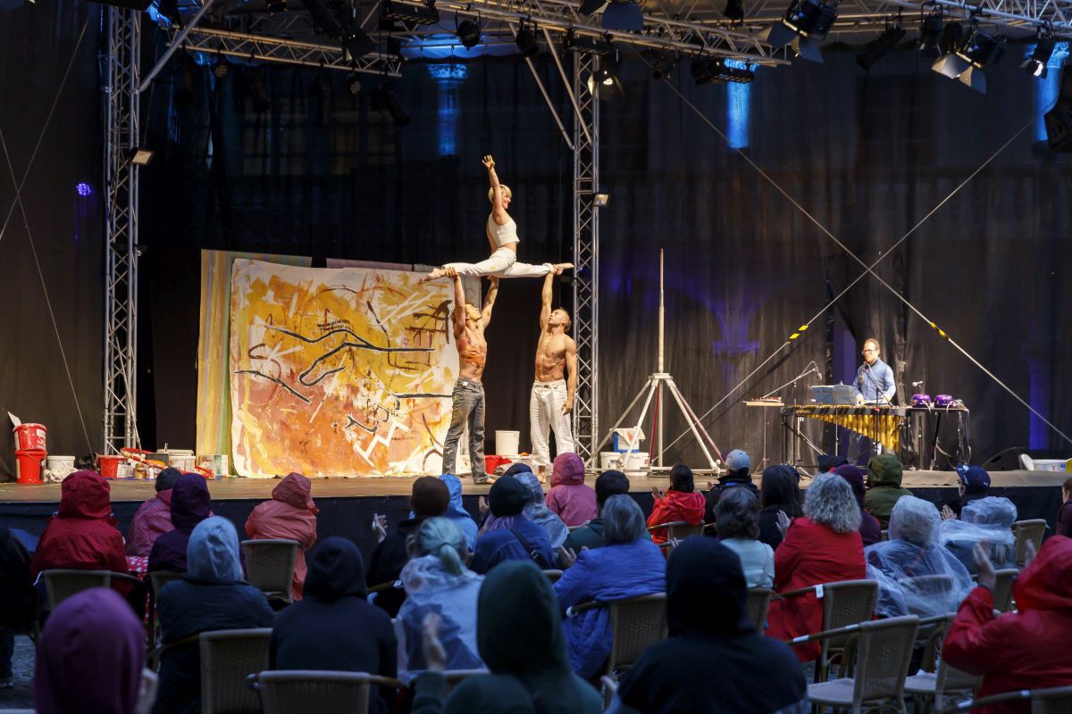 Fotografie – Akrobatikperformance auf der Bühne in Regensburg vor Publikum, Carmen Lück im Spagat in der Luft gestützt durch ihre beiden männlichen Akrobatikkollegen
