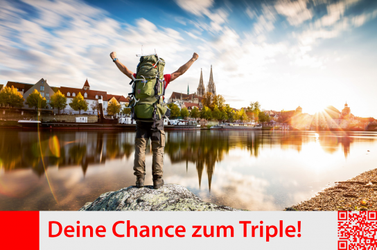 Mann mit großem Rucksack, Arme hoch reißend, Siegerpose; vor ihm die Donau und dahinter Blick auf Regensburg mit dem Dom; blauer Himmel mit weißen Wolken