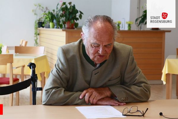 Ein Mann sitzt an einem Tisch und liest von einem Blatt.
