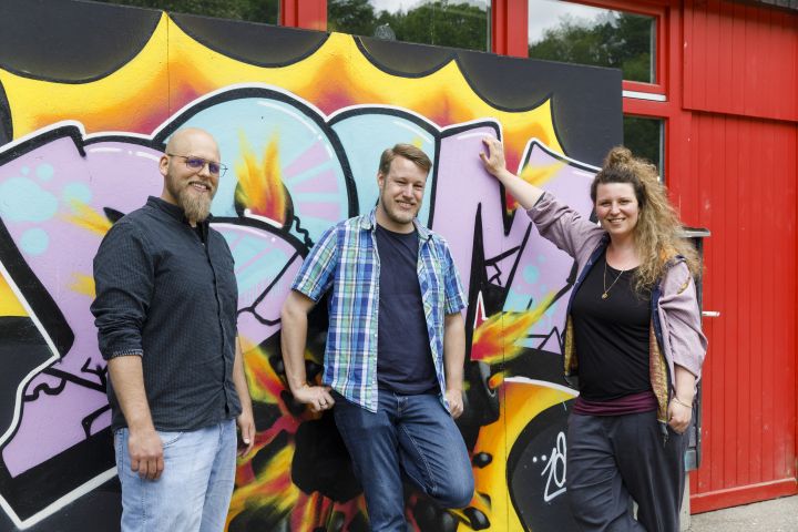 Das Team des Jugednzentrums (Benjamin Diestelmann, Lennart Krummeck und Esther Günther von links nach rechts) lehnt an einem Graffiti auf dem BOOM steht. (C) Stadt Regensburg JUZ Königswiesen - Team 2022 (Herbst)