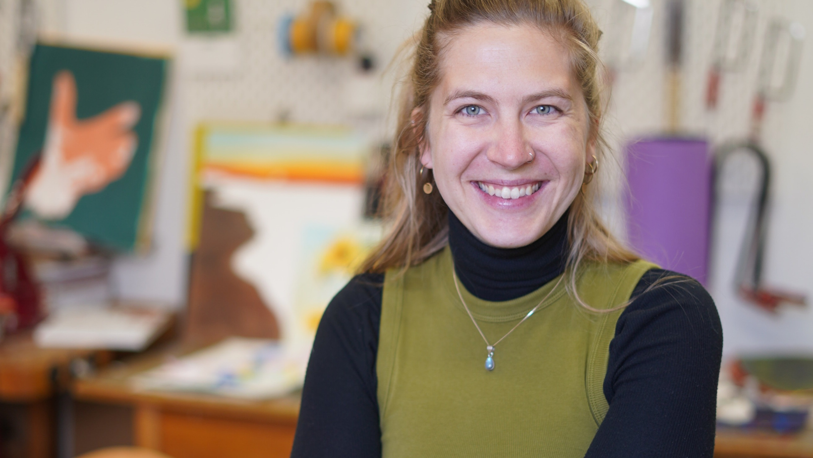 Man sieht auf dem Bild Sara Peßler im Atelier, der Hintergrund ist verschwommen und sie lächelt freundlich in die Kamera.
