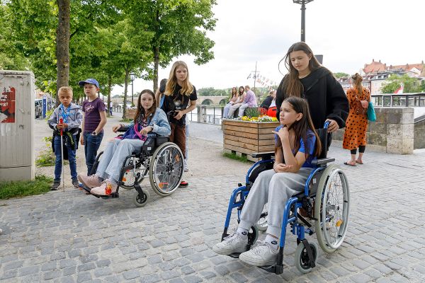 Fotografie - Kinder aus dem Kinderbeirat im Rollstuhl sitzend oder mit Langstock werden von anderen Mitgliedern des Kinderbeirates begleitet