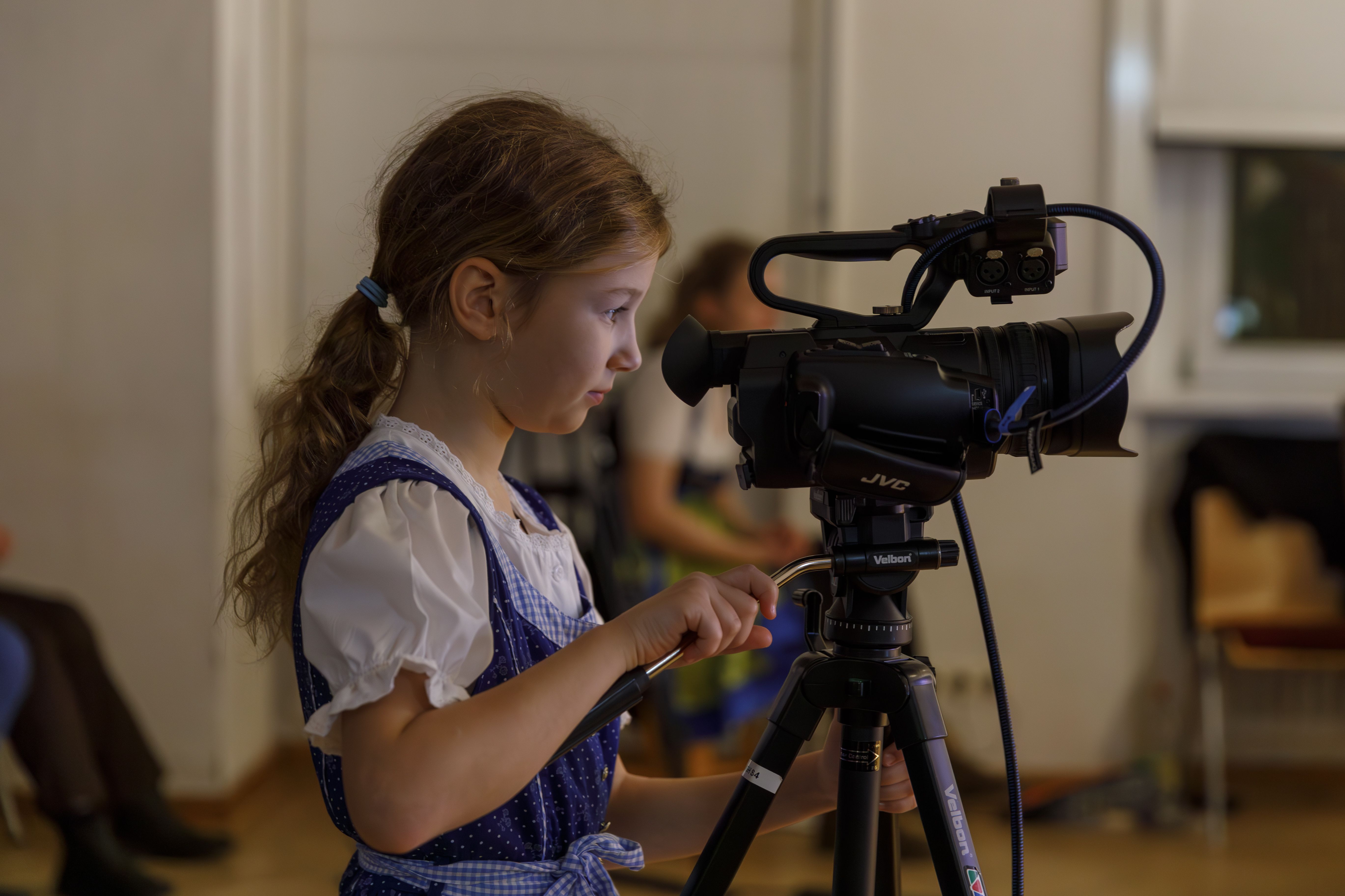 Mädchen im Dirndl schaut durch eine Filmkamera