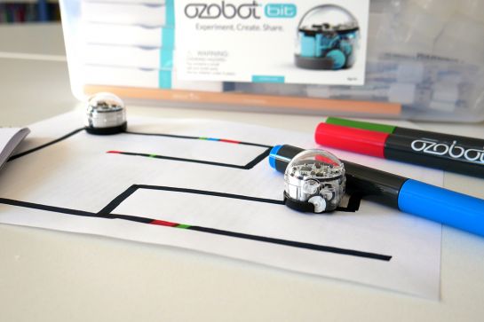 Foto von zwei Ozobotrobotern, einer Box und drei Stiften