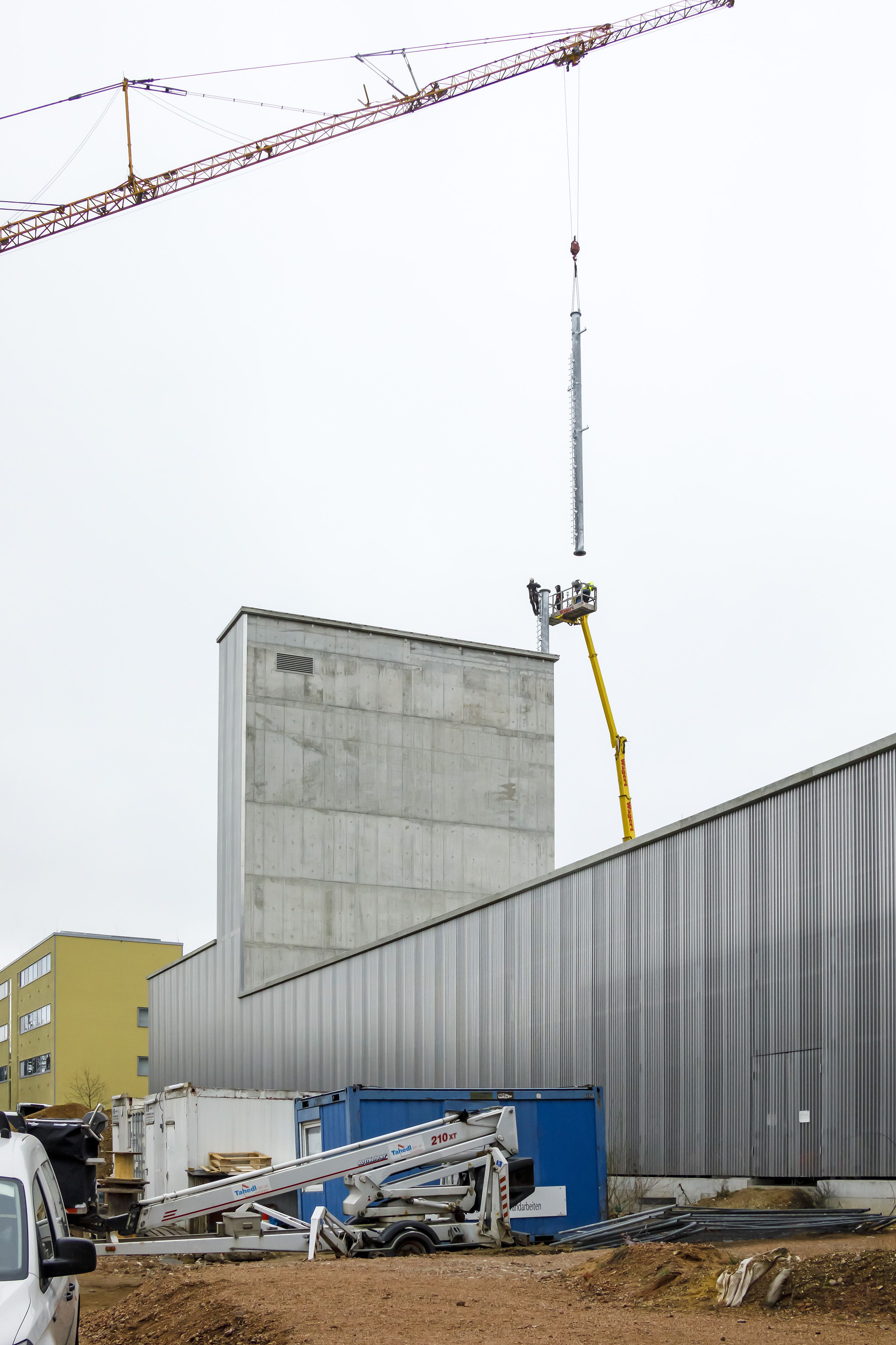 Fotografie - Montage des Funkmastes am Schlauchturm - Teil des Funkmastes schwebt mittels eines Krans zur Montage über dem Schlauchturm