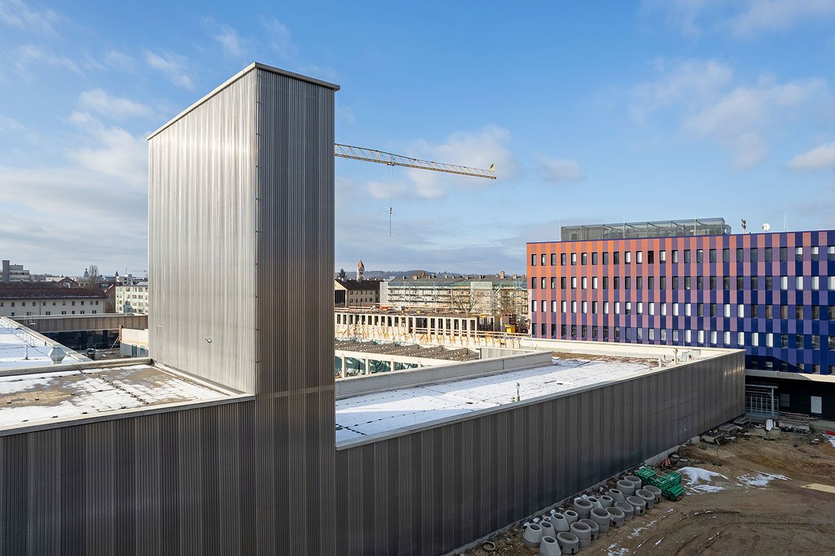 Fotografie - im Hintergrund Rohbau ist der Fahrzeughalle zu sehen, rechts davon der Neubau der Hauptfeuerwache; im Vordergrund bereits fertiggestellte Fahrzeughalle mit Schlauchturm