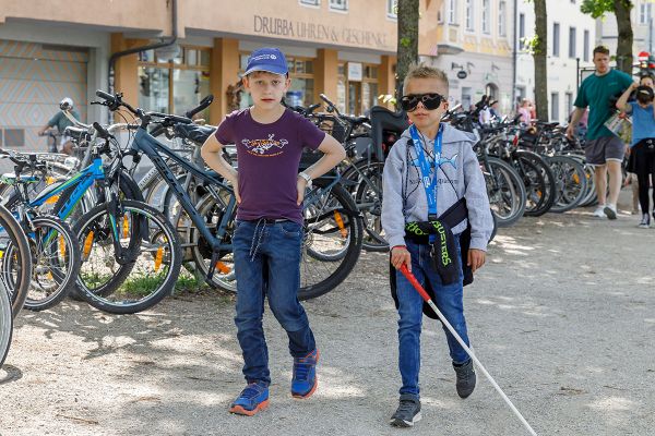 Fotografie - Zwei Jungen aus dem Kinderbeirat mit Langstock und einer Brille, die eine Sehbehinderung simuliert