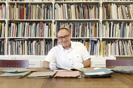Fotografie: Dr. Roman Smolorz sitzt vor Recherchedokumenten. (C) Bilddokumentation Stadt Regensburg