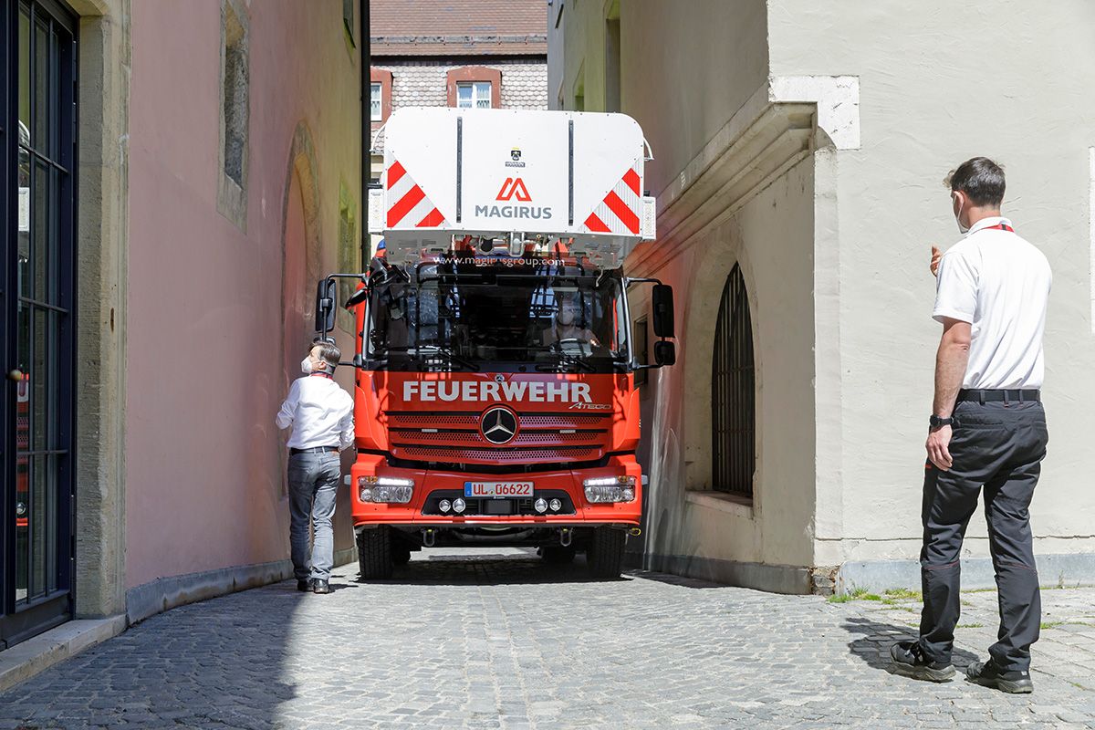 Fotografie: Ein Leiterwagen der Feuerwehr in einer engen Altstadtgassen, zwei Männer geben Anweisungen.