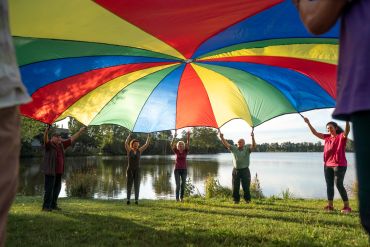 Fotografie: Seniorinnen und Senioren schwingen ein Schwungtuch vor einem See.
