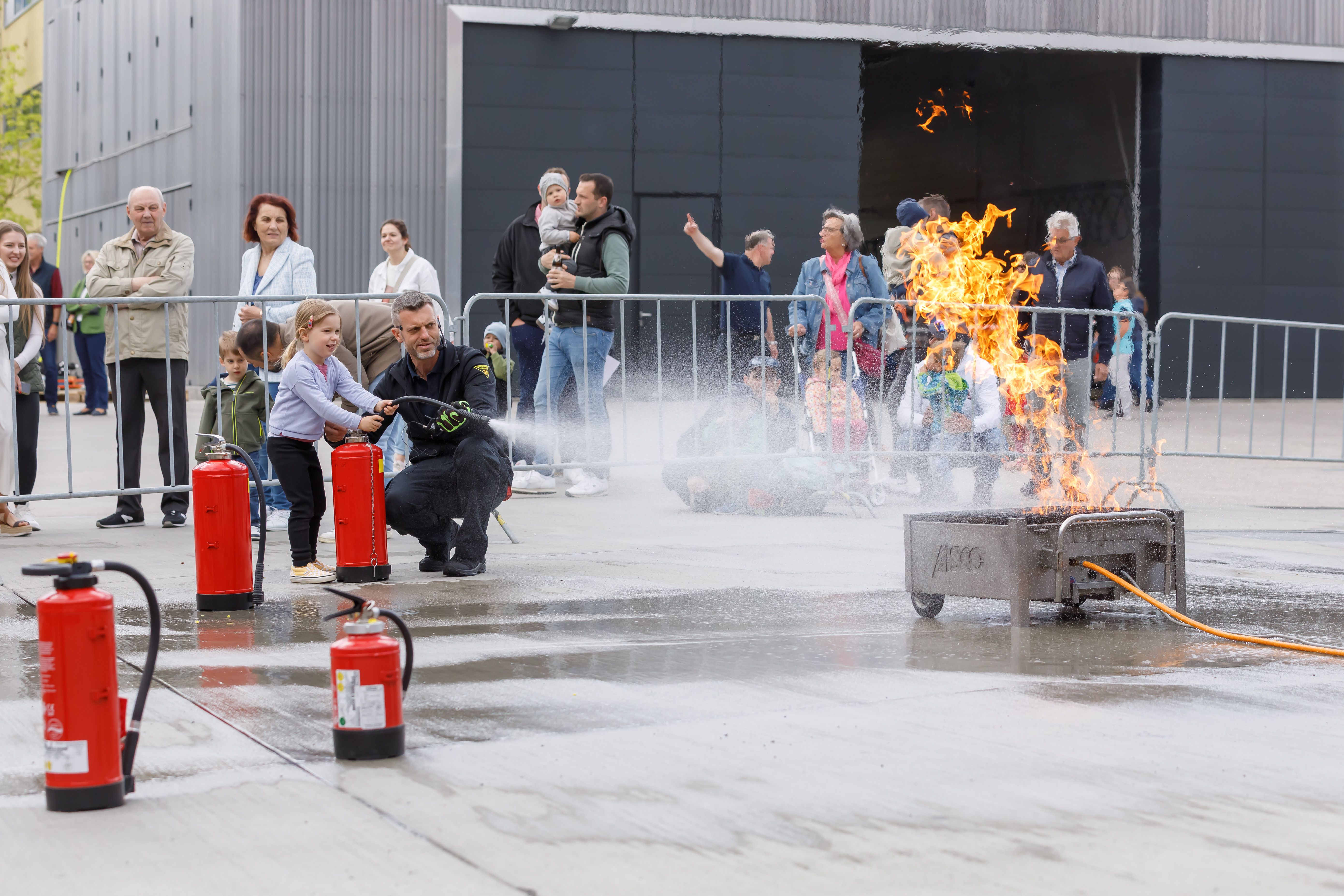 Fotografie: Ein Kind löscht mit einem Feuerwehrler ein Feuer mit dem Feuerlöscher.
