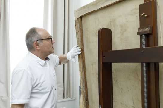 Fotografie: Dr. Roman Smolorz zeigt eine Registraturnummer auf der Rückseite eines Gemäldes.